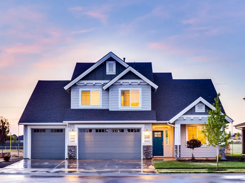 Two-story craftsman home with new dark charcoal asphalt shingle roof and stone accents, photographed at dusk after full replacement