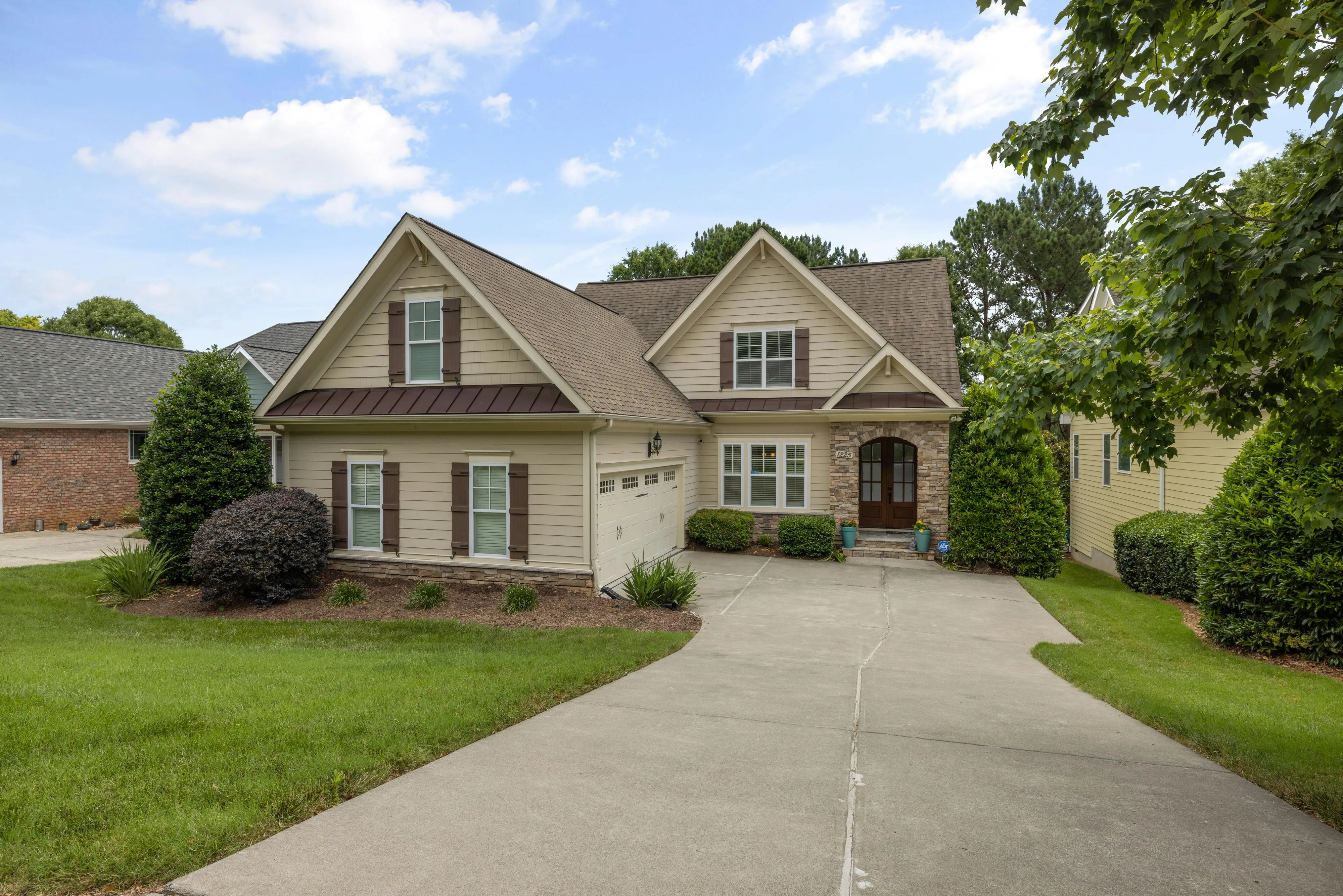 Craftsman-style home with tan siding, stone accents, and newly installed brown metal accent roofing over the garage