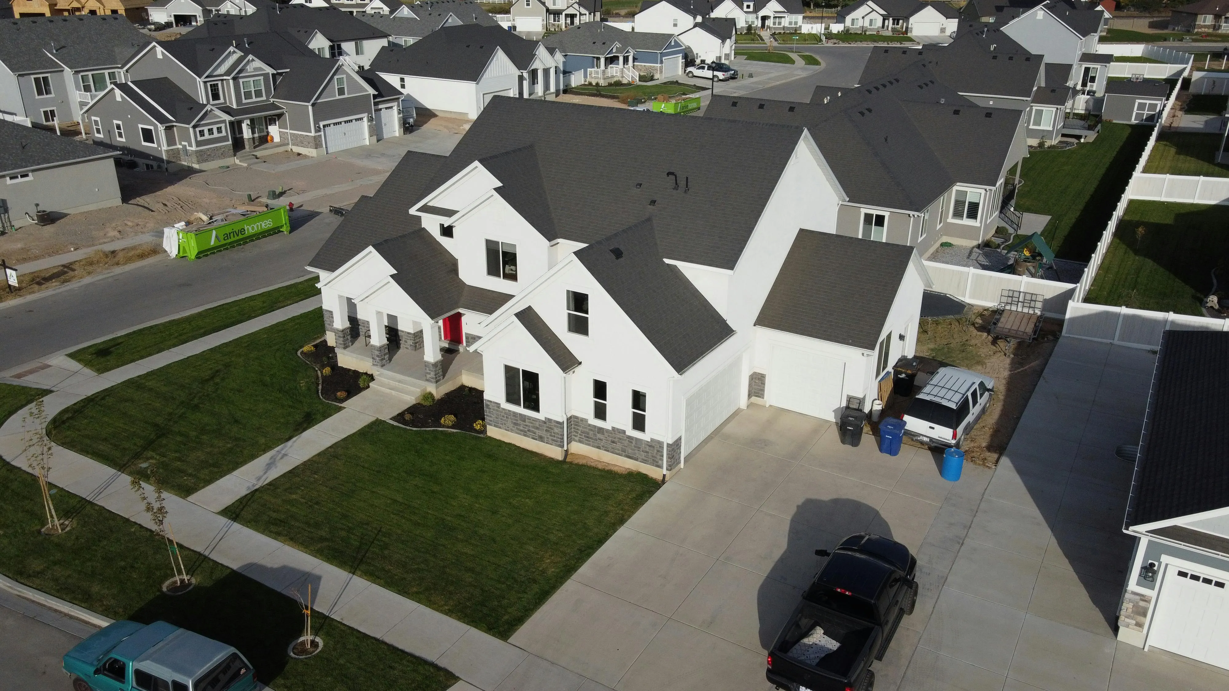 Aerial view of a large modern farmhouse with white siding and dark gray asphalt shingles, showing the full roofline after installation