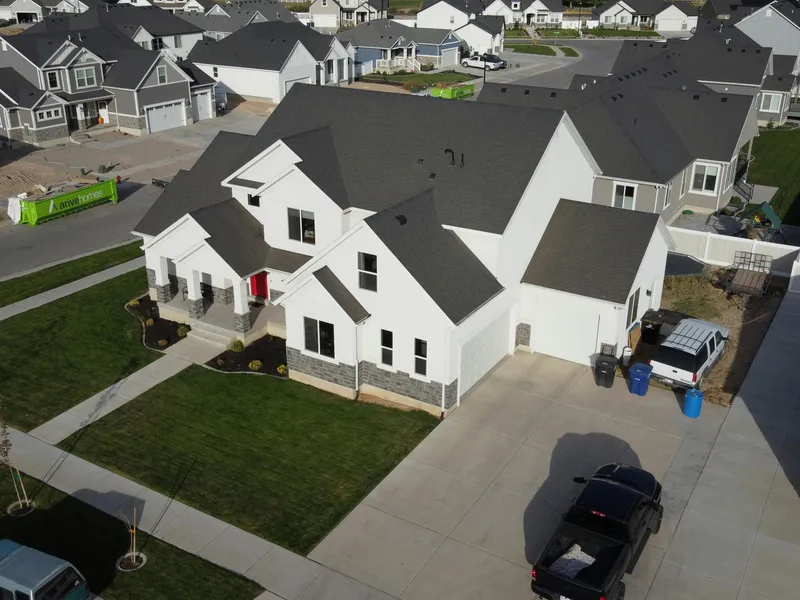 Aerial view of a large modern farmhouse with white siding and dark gray asphalt shingles, showing the full roofline after installation