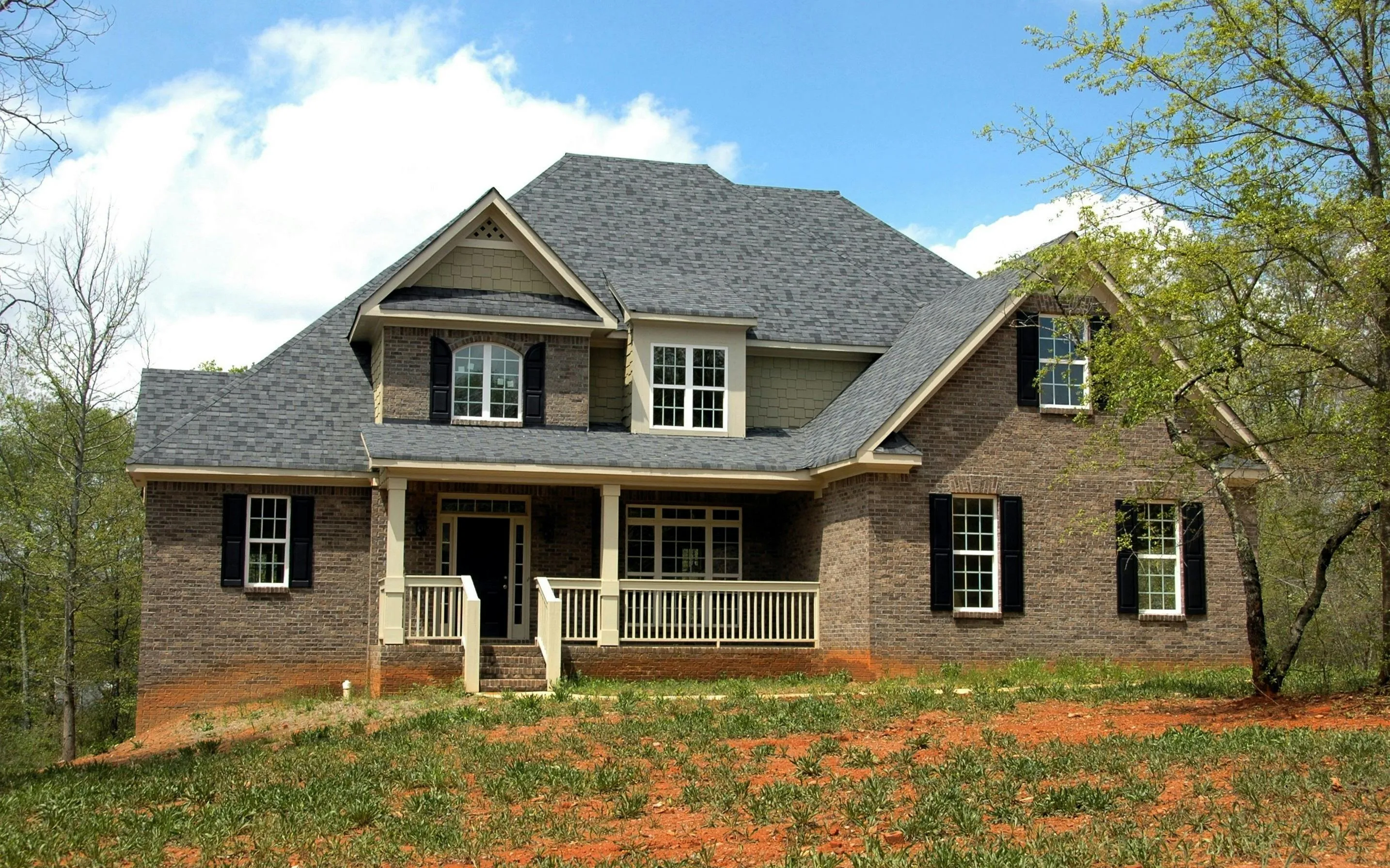 Brick two-story colonial home with new gray architectural shingles and white front porch, completed residential roof replacement