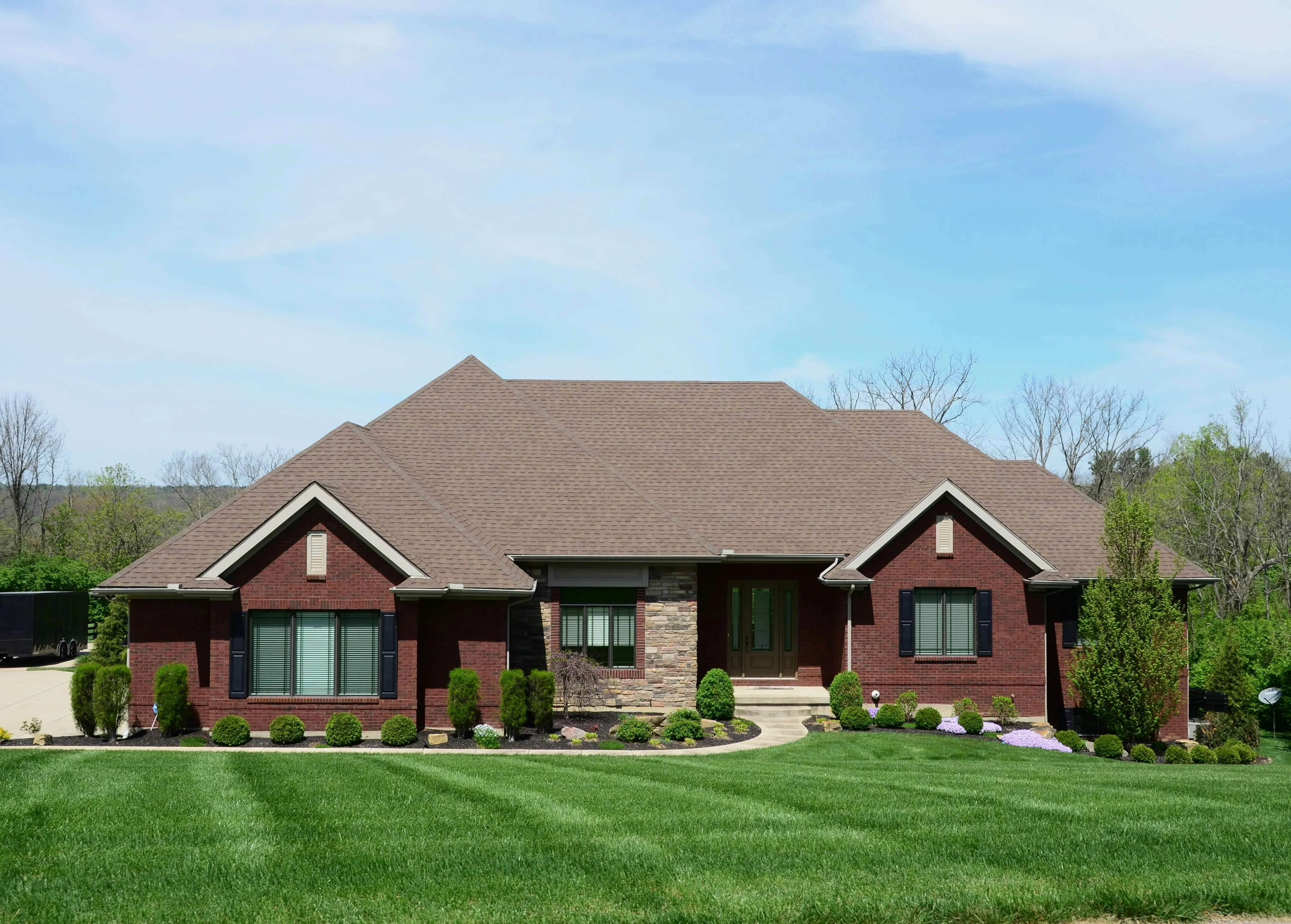 Single-story brick ranch home with new brown architectural shingle roof and stone accent facade, photographed after full roof installation