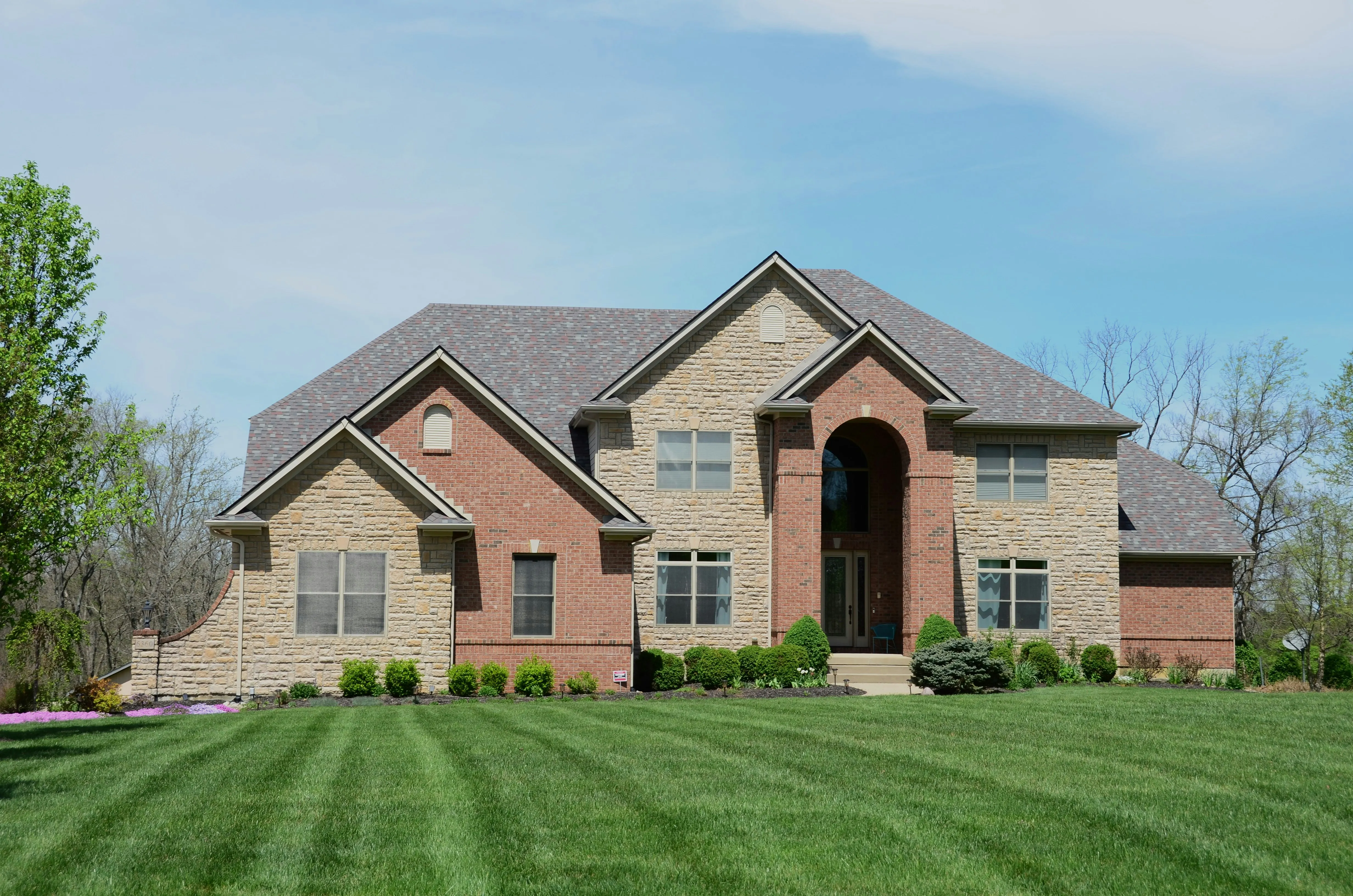 Two-story brick and stone colonial home with new gray architectural shingle roof and arched entry, completed roof replacement project