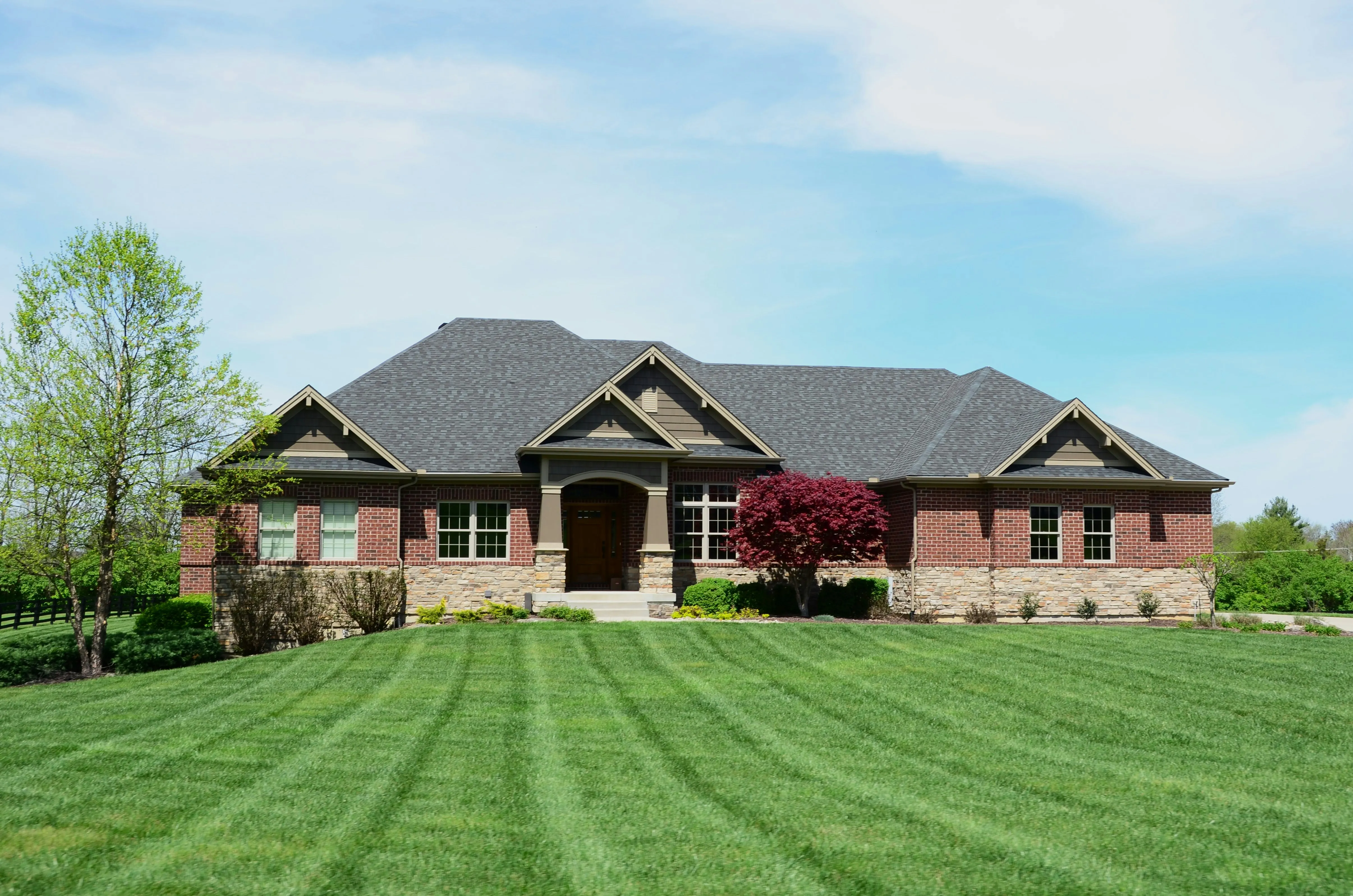 Single-story brick craftsman home with new dark charcoal architectural shingle roof and manicured lawn, completed residential roofing project