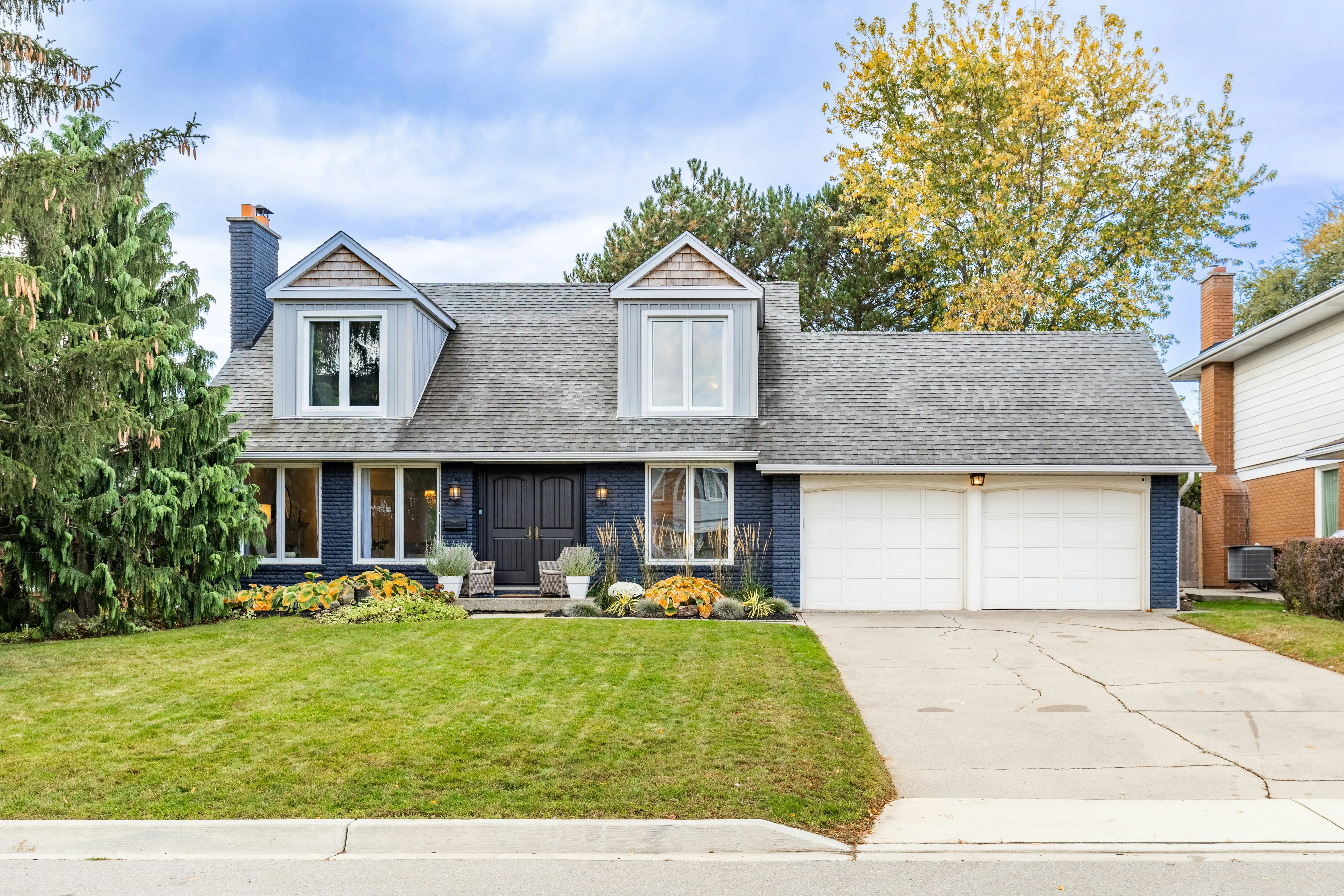 Cape Cod style home with navy blue siding and new gray asphalt shingle roof with dormers, photographed in autumn after full roof replacement